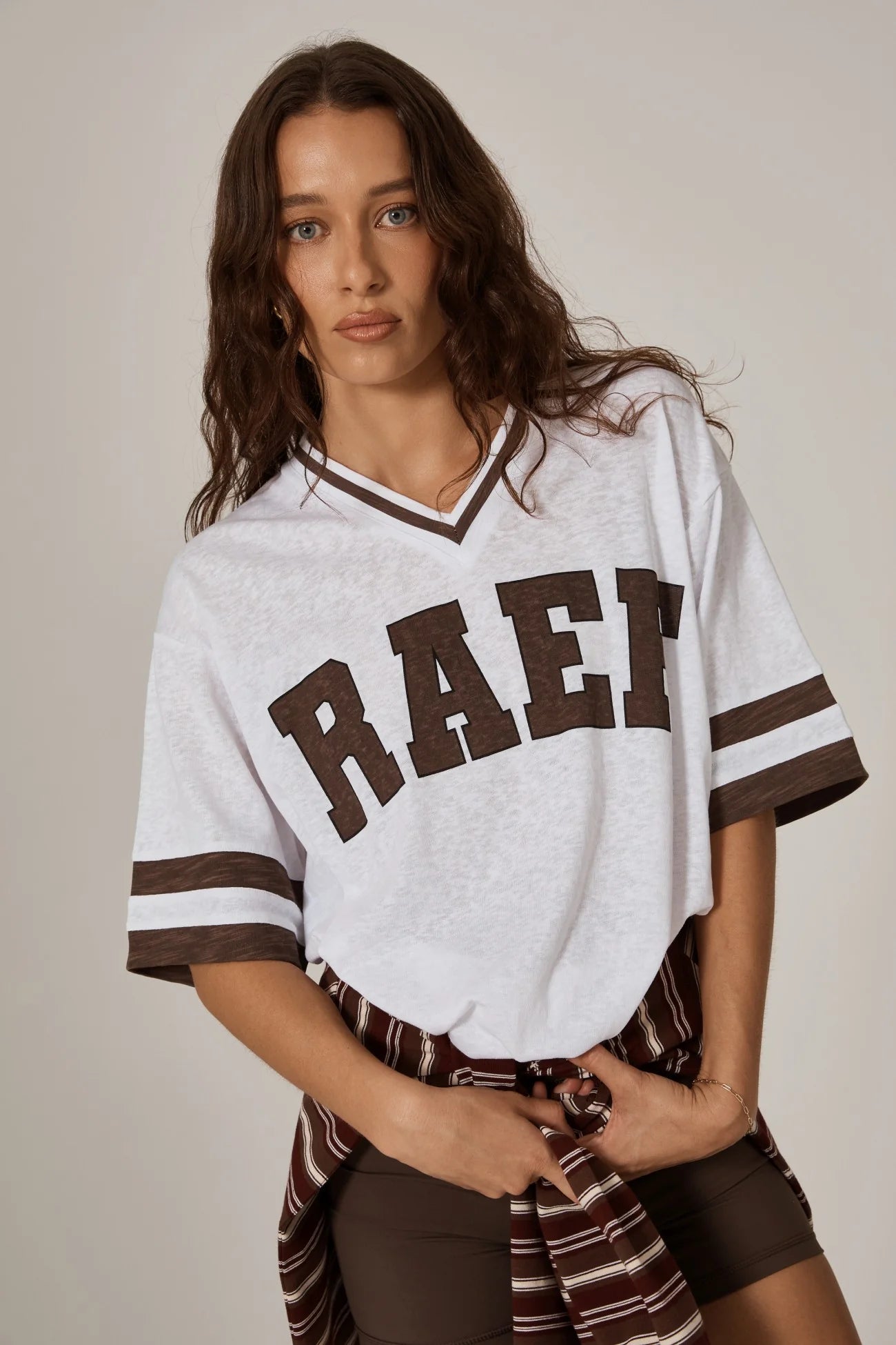 Woman standing in a cool girl white oversized tee with brown graphics and a stripe sweater around her waist