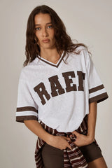 Woman standing in a cool girl white oversized tee with brown graphics and a stripe sweater around her waist