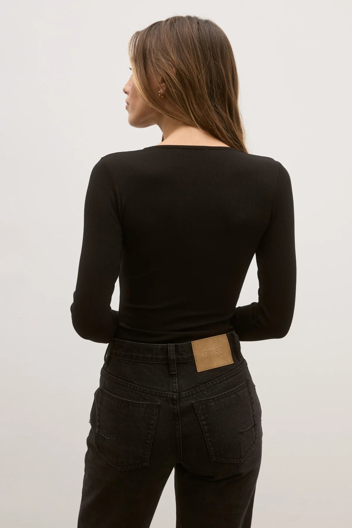 Person wearing a black long-sleeve top and dark jeans on a plain background