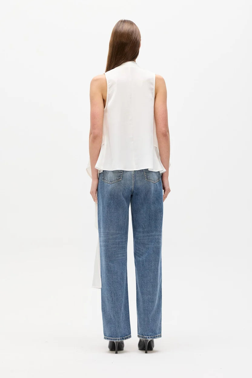 A woman viewed from behind wearing a sleeveless white top and wide-leg blue jeans against a plain white studio background.