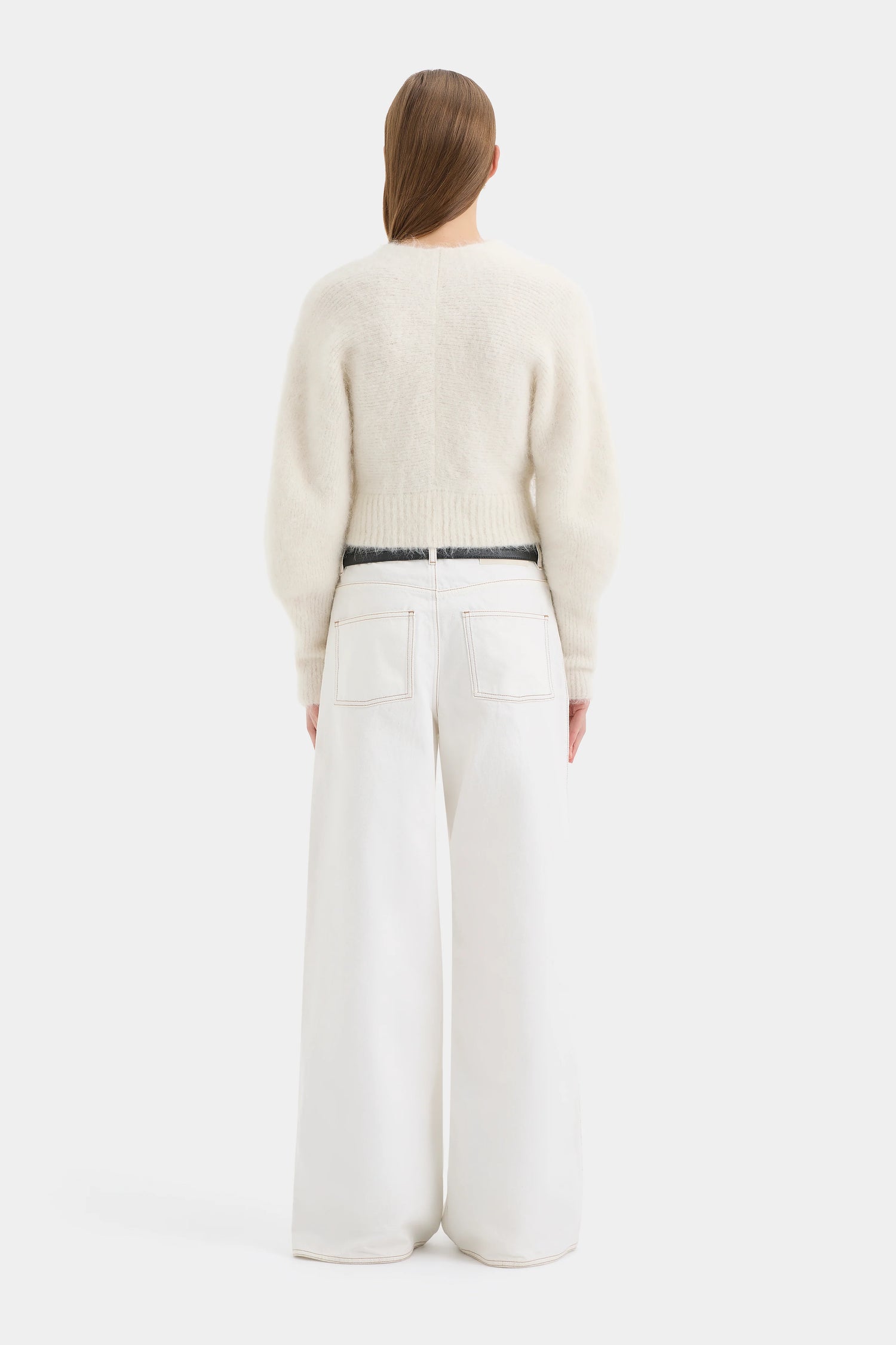 Person wearing a cream sweater and white pants on a white background