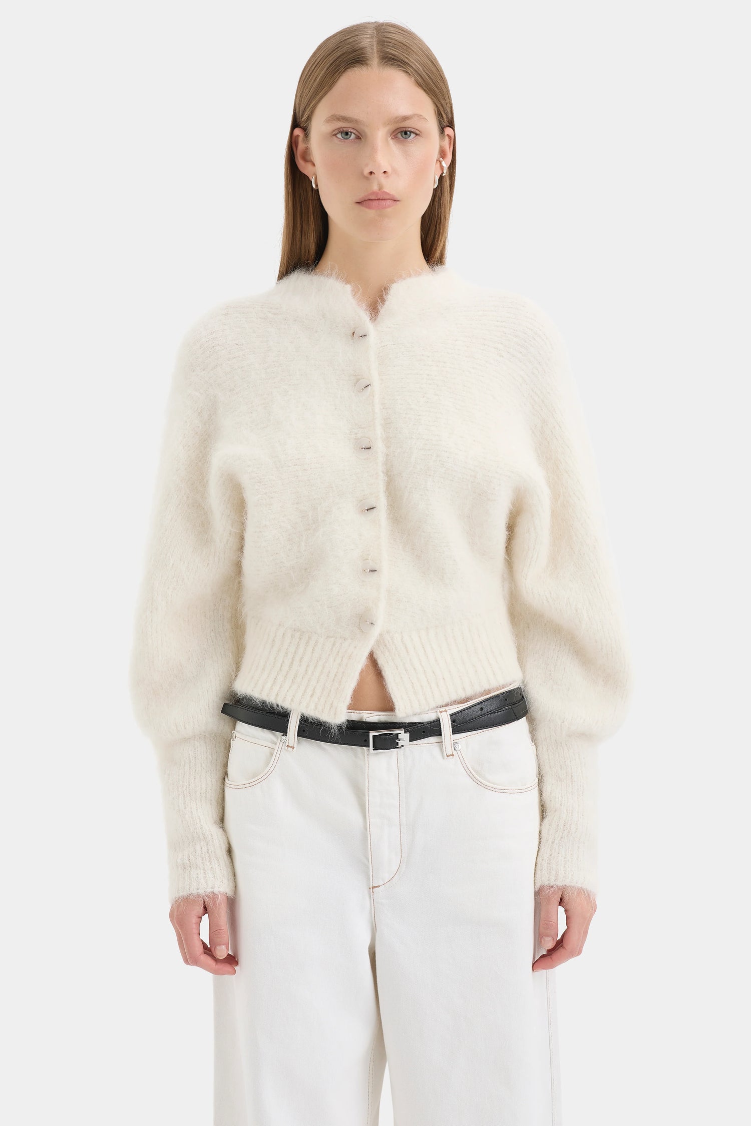 Woman wearing a cream cardigan and white pants on a white background