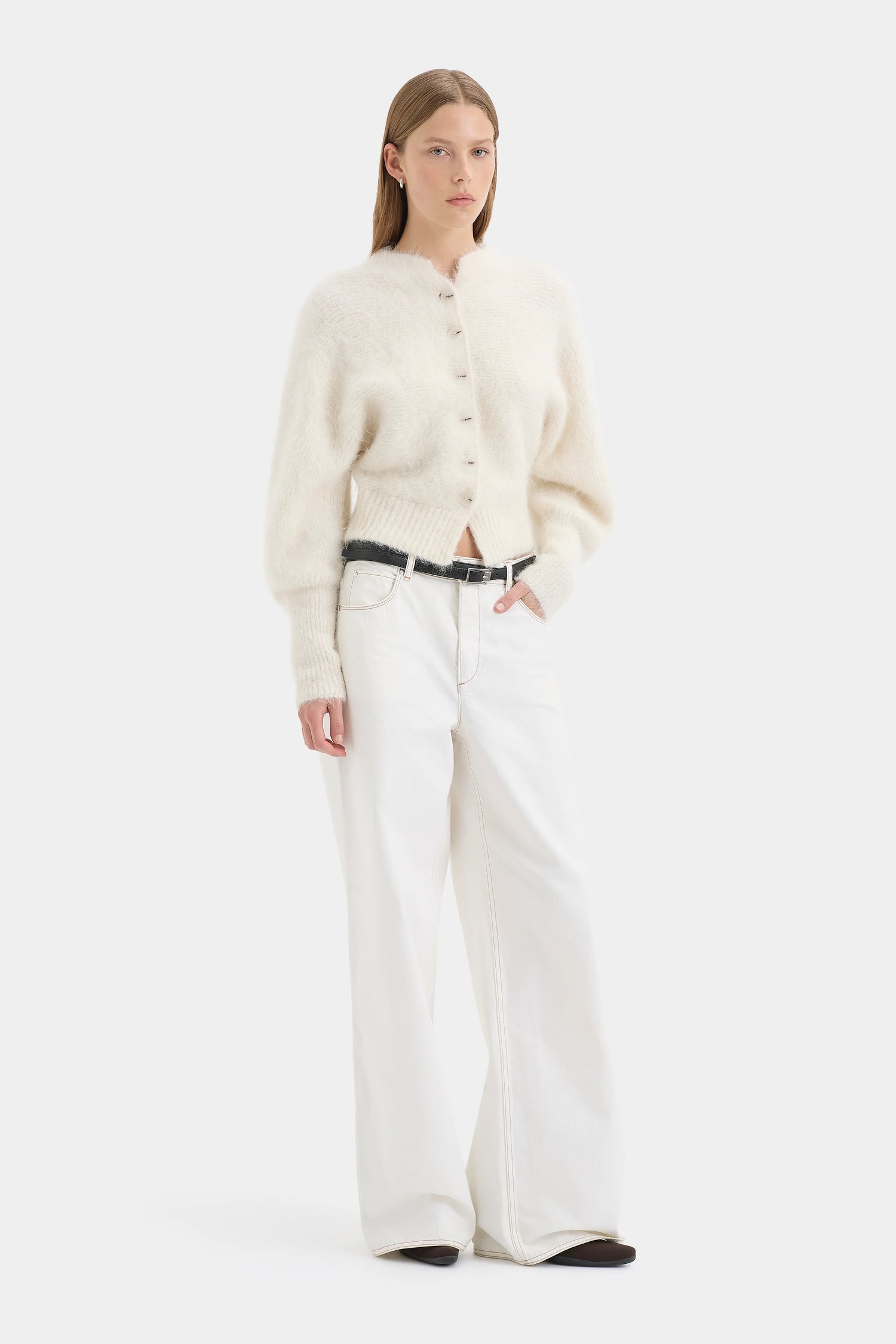 Woman wearing a cream-colored button-up shirt and white pants on a white background