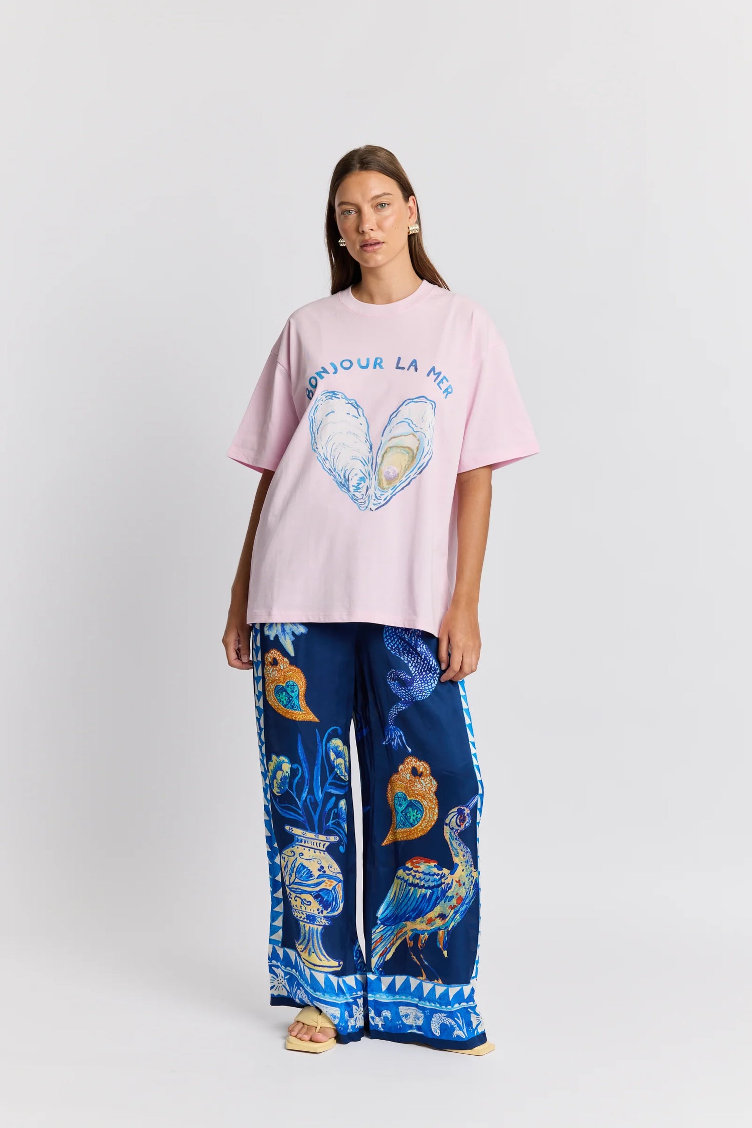 Woman wearing a pink oversized t-shirt with a graphic design and blue patterned pants on a white background