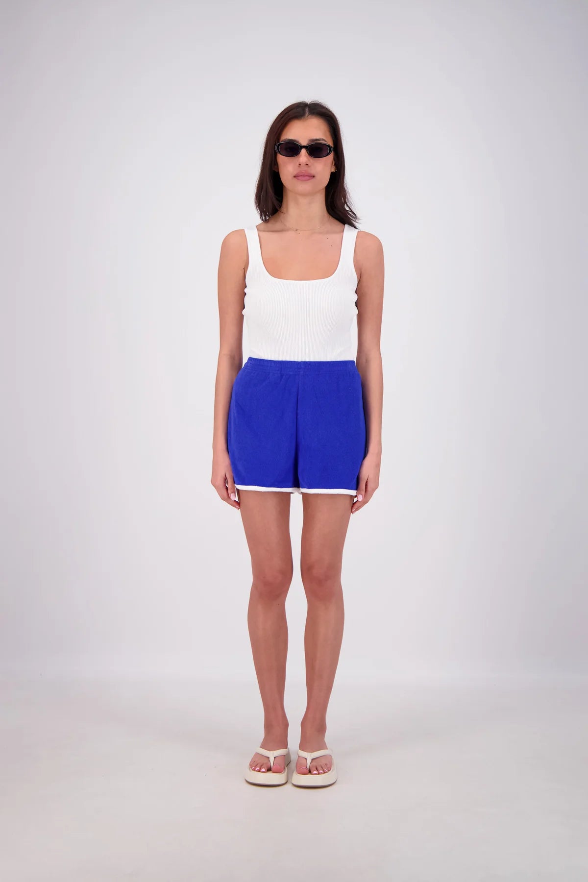 Woman wearing a white tank top and blue shorts on a plain background