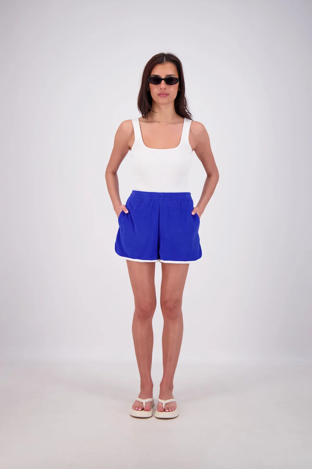 Woman wearing a white tank top and blue shorts on a white background