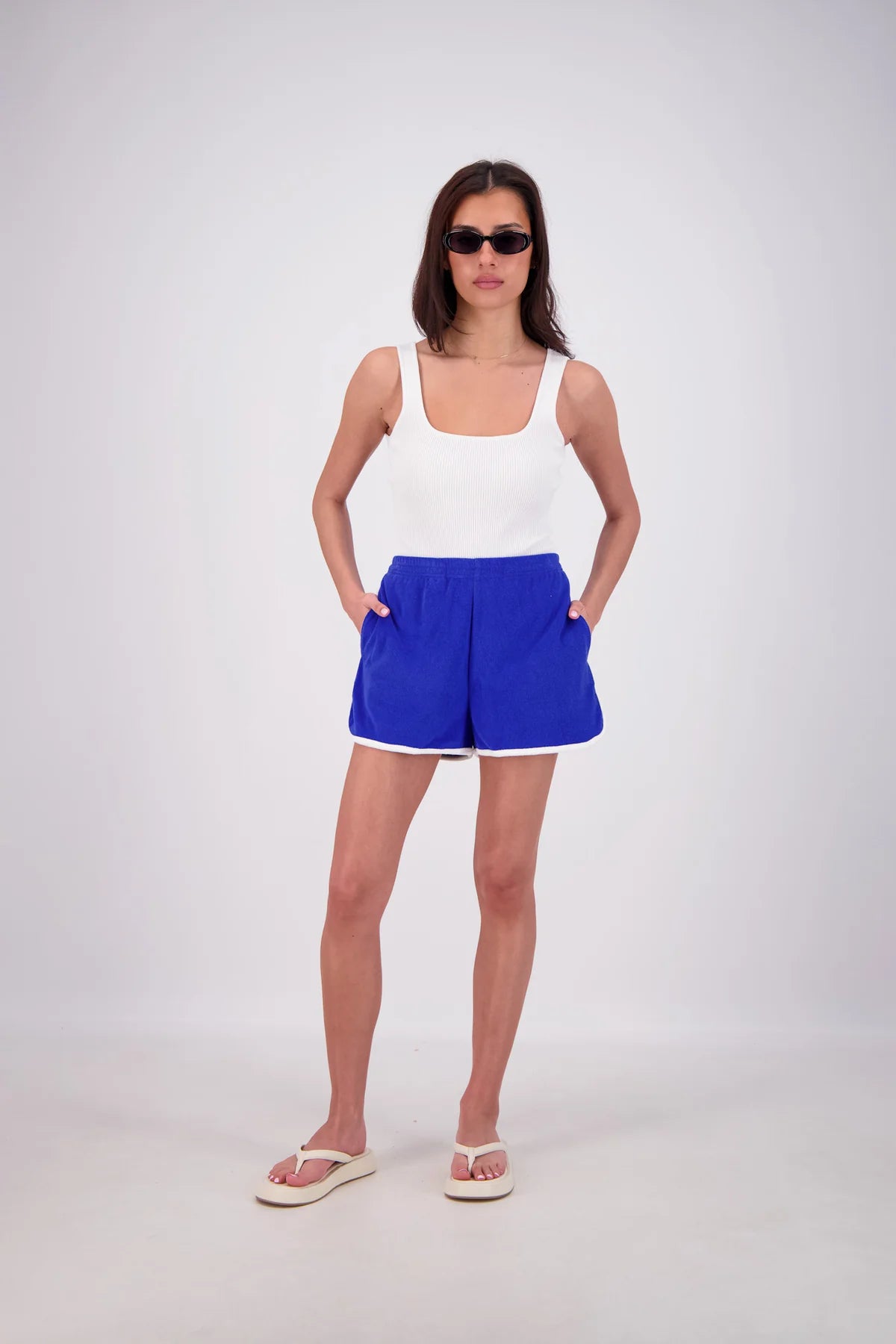 Woman wearing a white tank top and blue shorts on a white background