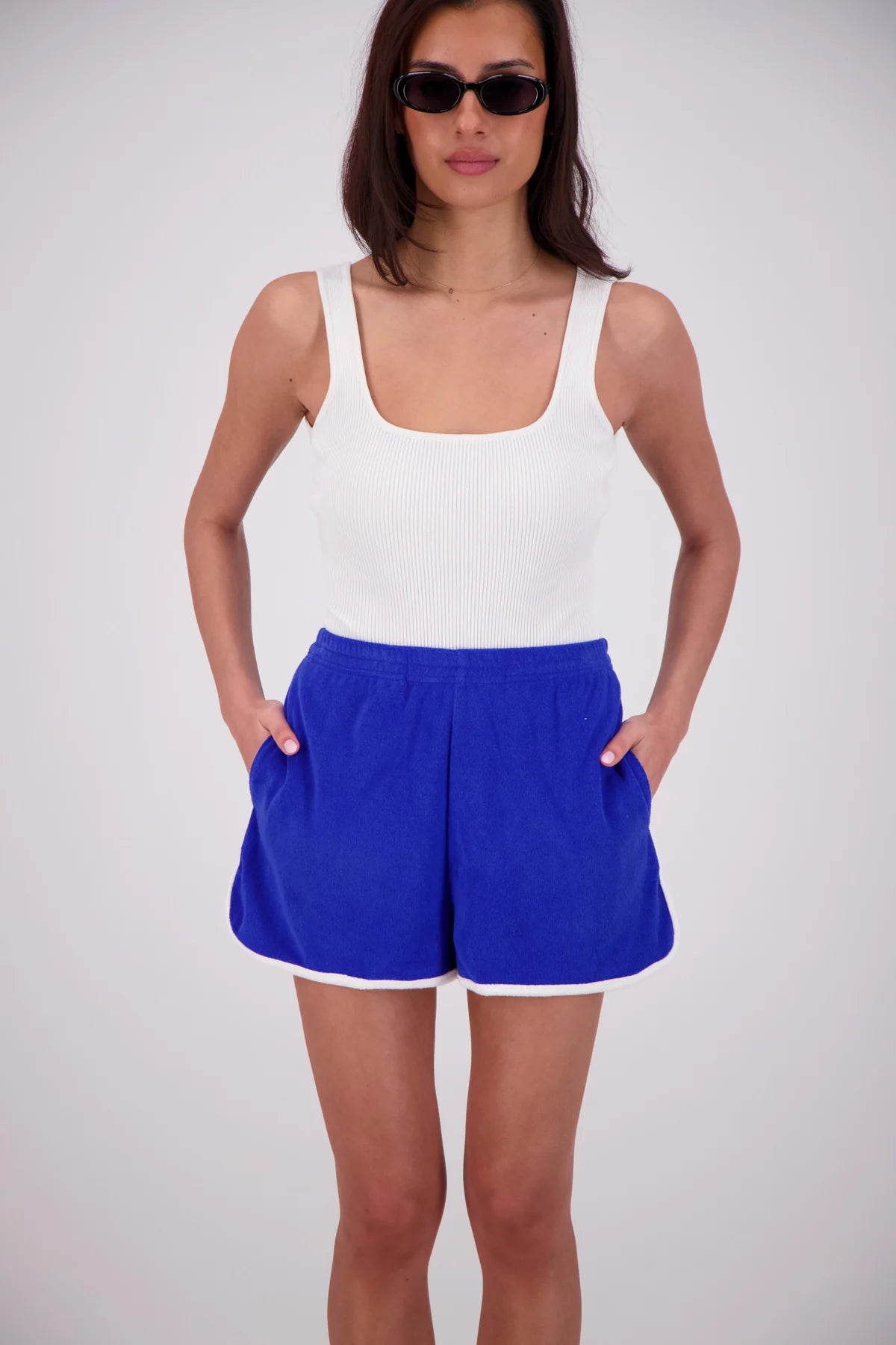 Woman wearing a white tank top and blue shorts on a plain background