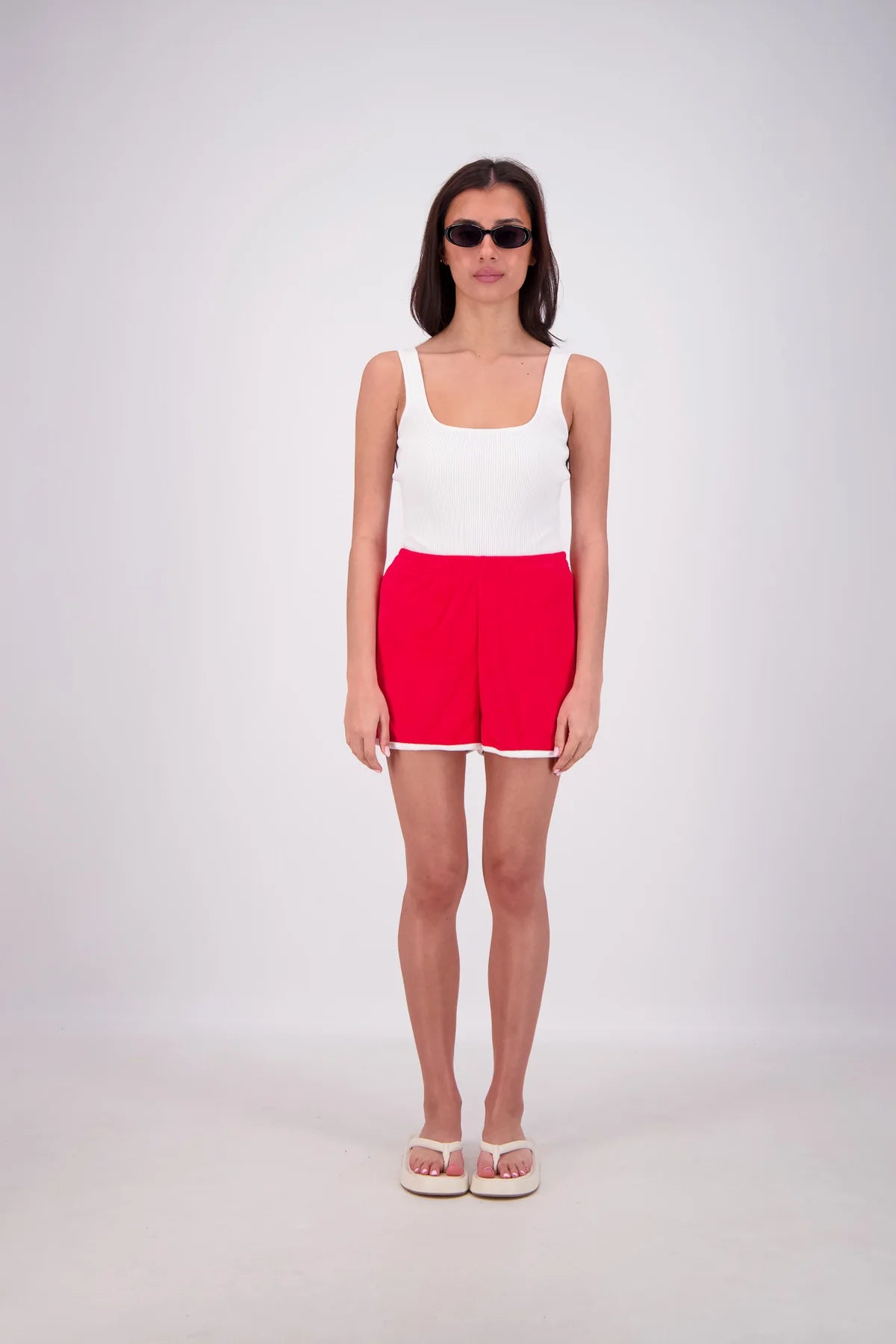 Woman wearing a white tank top and red shorts on a white background