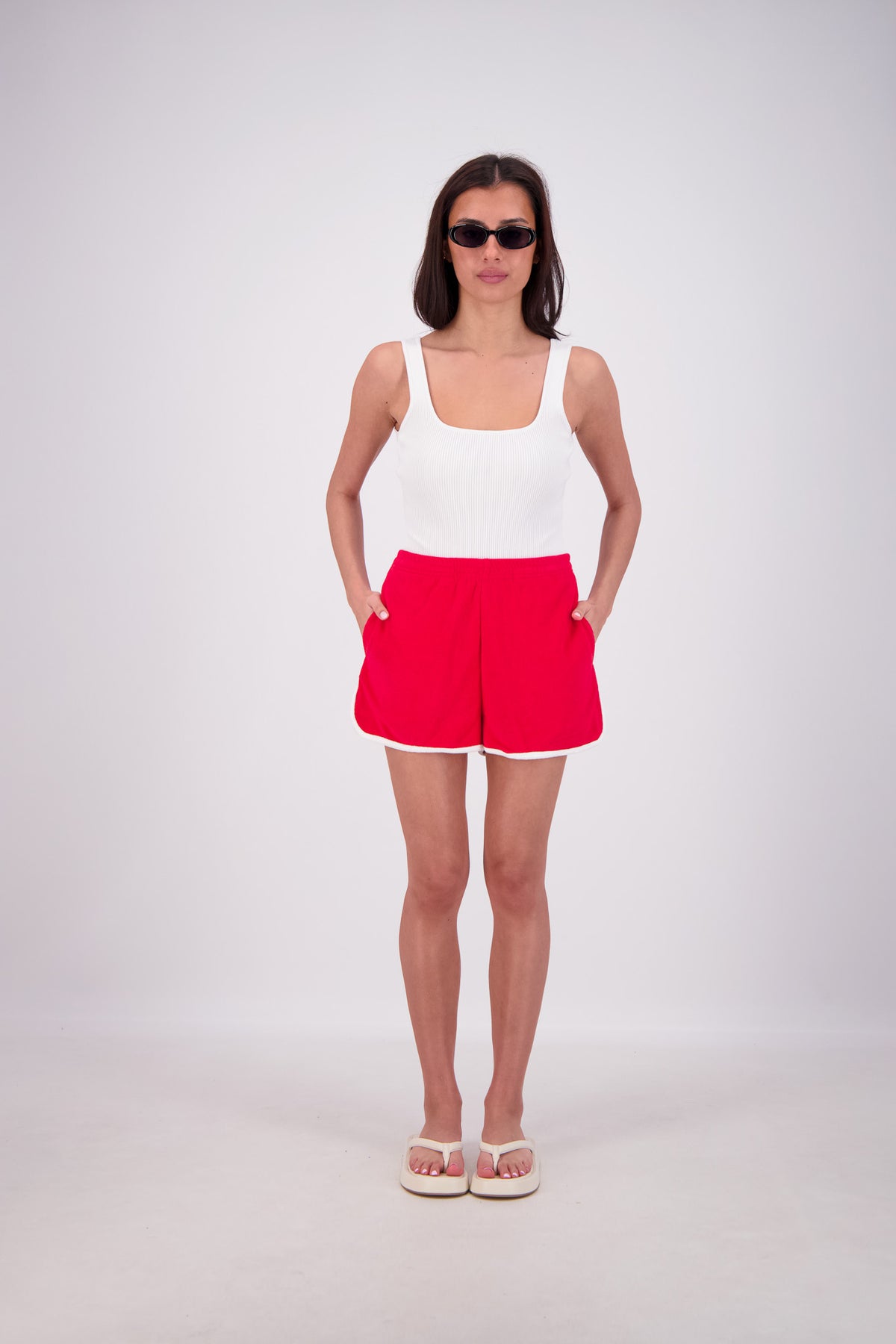 Woman wearing a white tank top and red shorts on a white background