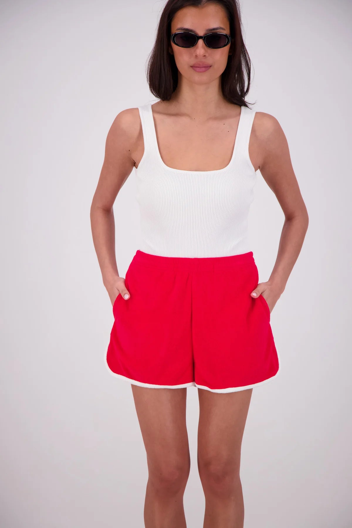 Woman wearing a white tank top and red shorts on a plain background