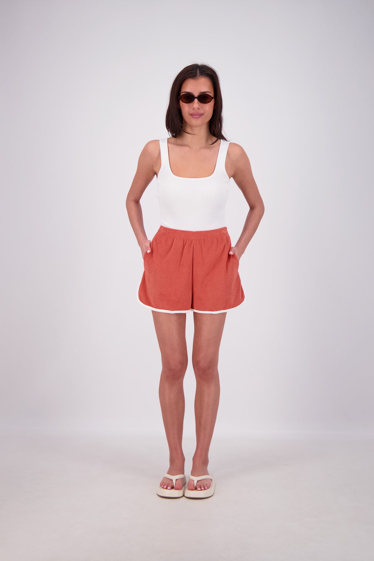Woman wearing a white tank top and red shorts on a white background
