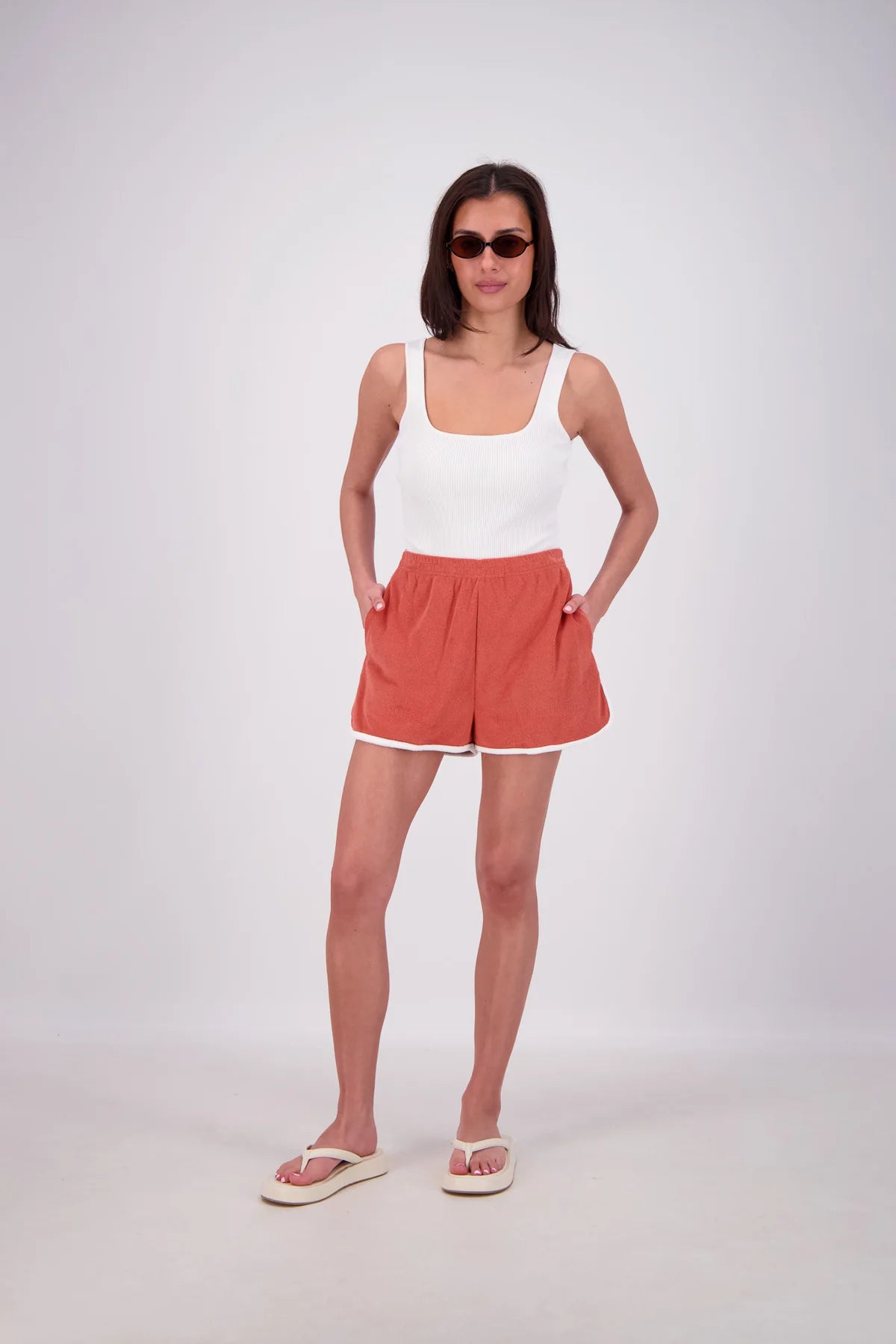Woman wearing a white tank top and red shorts on a white background