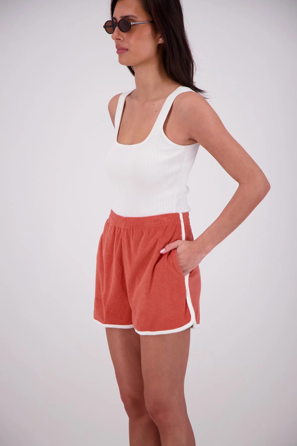 Woman wearing a white tank top and red shorts on a plain background