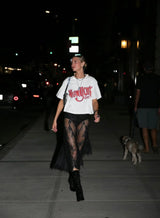 Person walking on a street at night wearing a white t-shirt with red text and black sheer stockings.
