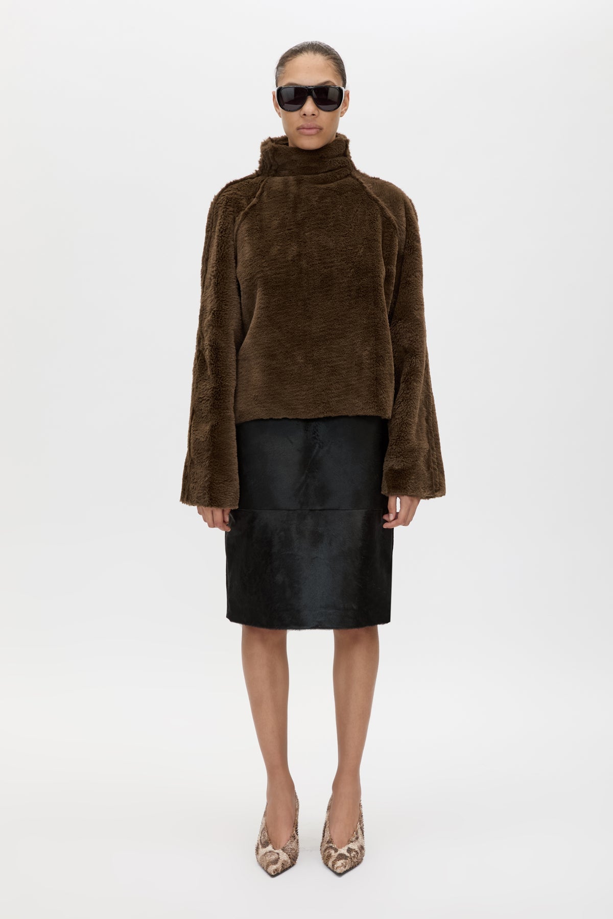 Person wearing a brown textured sweater and black skirt on a white background