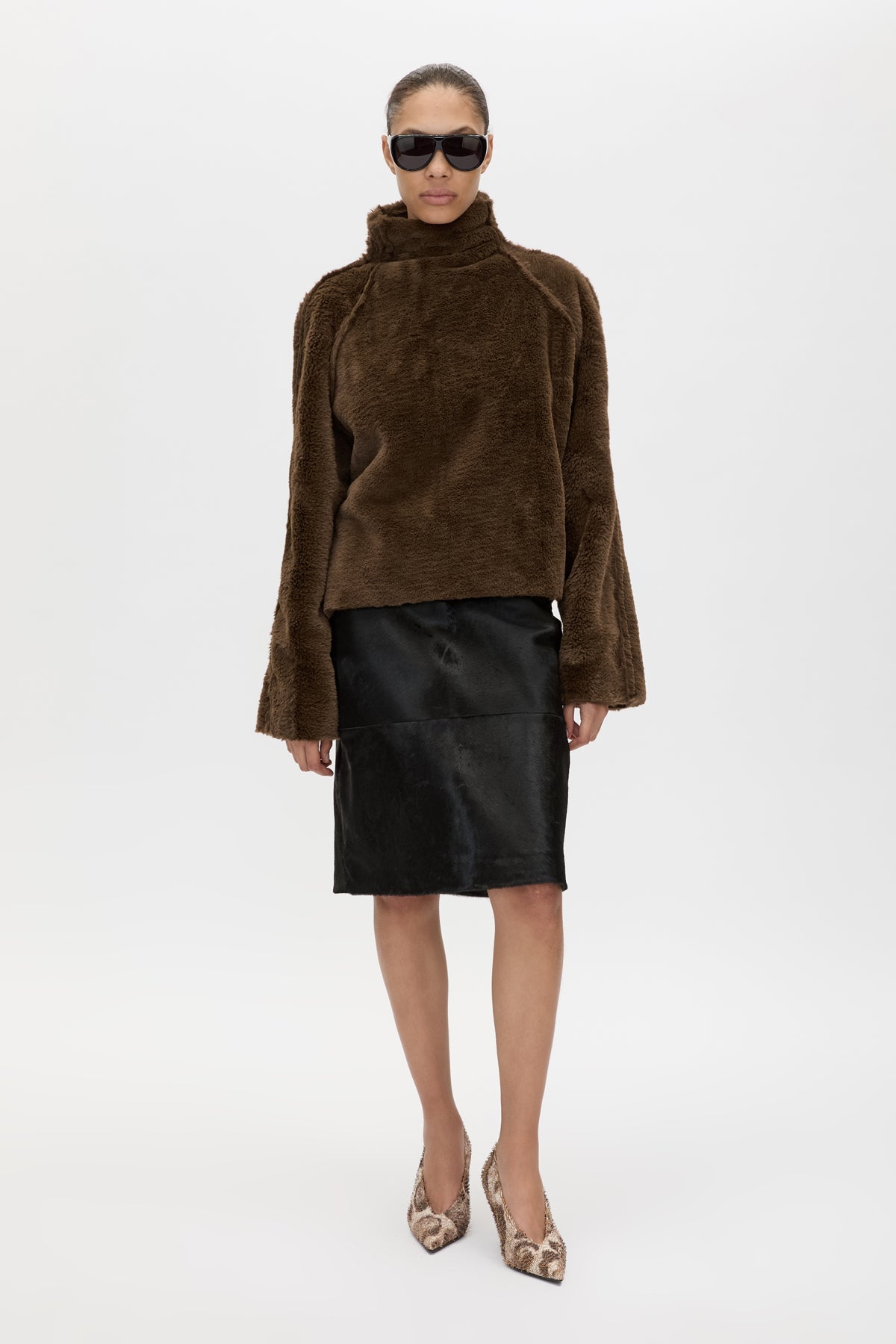 Person wearing a brown faux fur sweater and black leather skirt on a white background