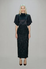 Woman wearing a black top and black textured skirt on a gray background