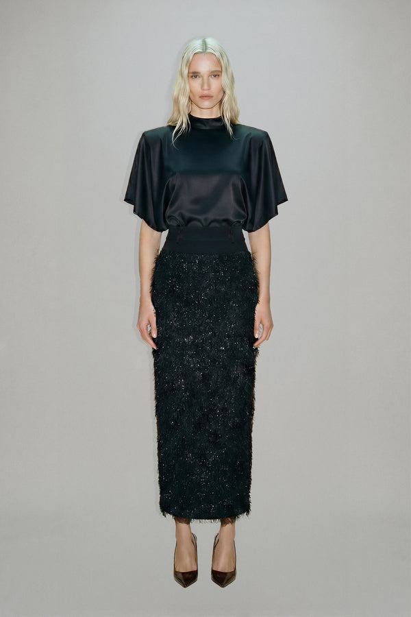 Woman wearing a black top and black textured skirt on a gray background