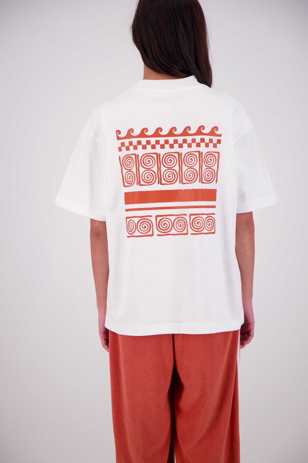 Person wearing a white t-shirt with red patterns on the back, standing against a plain background.