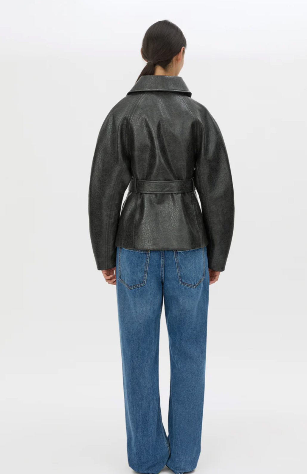 Person wearing a dark gray jacket and blue jeans on a white background
