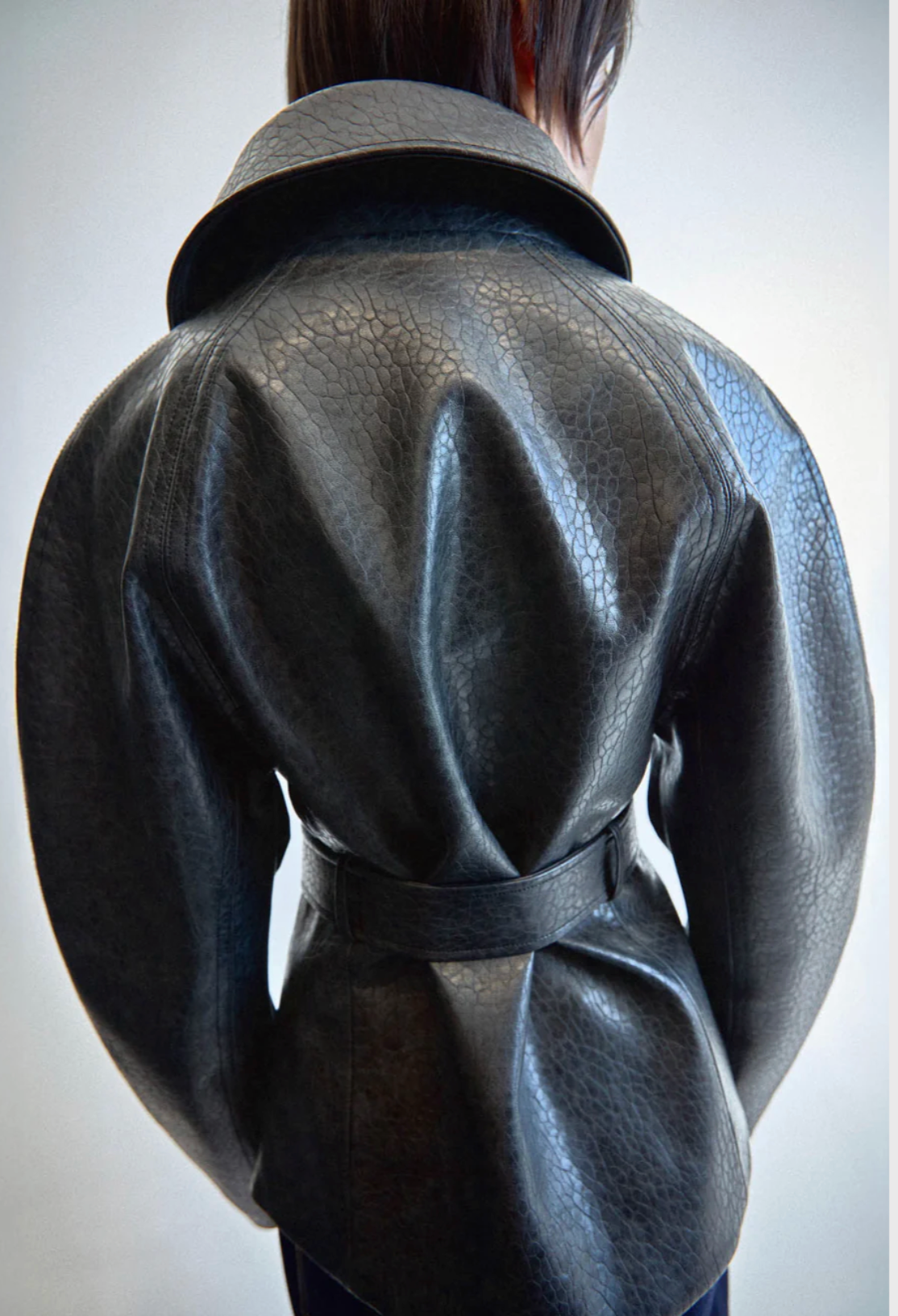 Back view of a person wearing a textured black leather jacket on a plain background
