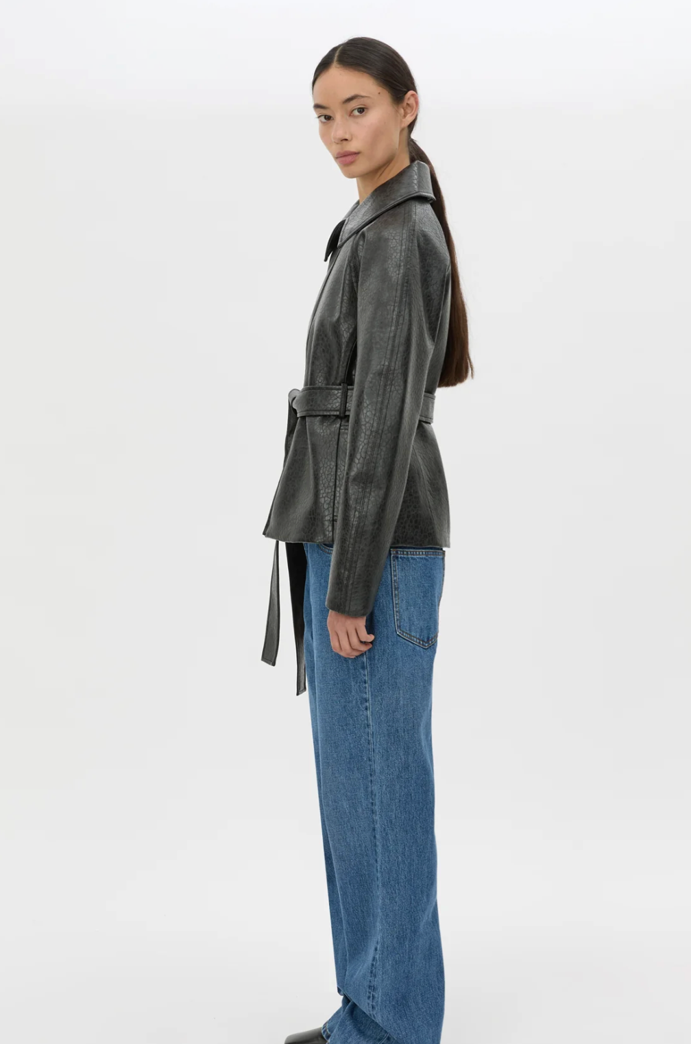 Woman wearing a grey leather jacket and blue jeans on a white background
