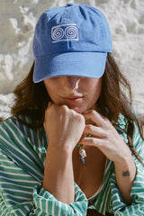 Person wearing a blue cap with a logo, sitting against a natural background