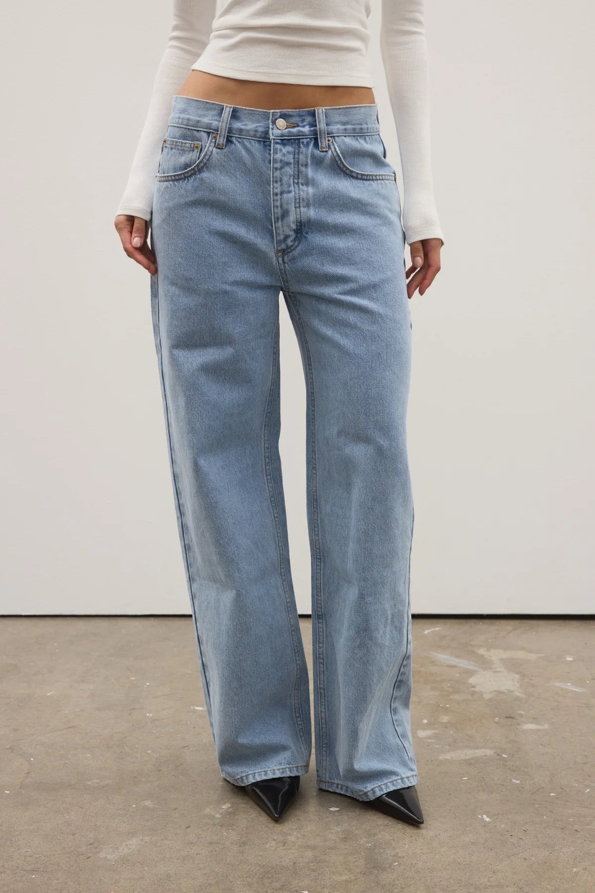 Person wearing light blue jeans and a white top against a plain background