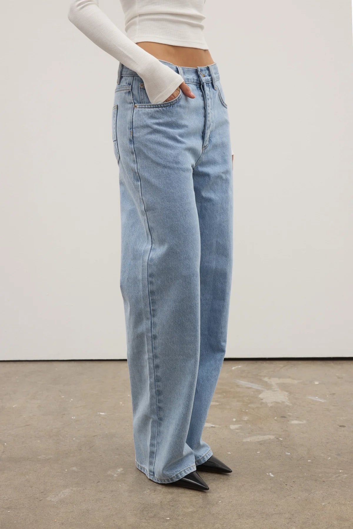 Person wearing light blue jeans and a white top against a plain background