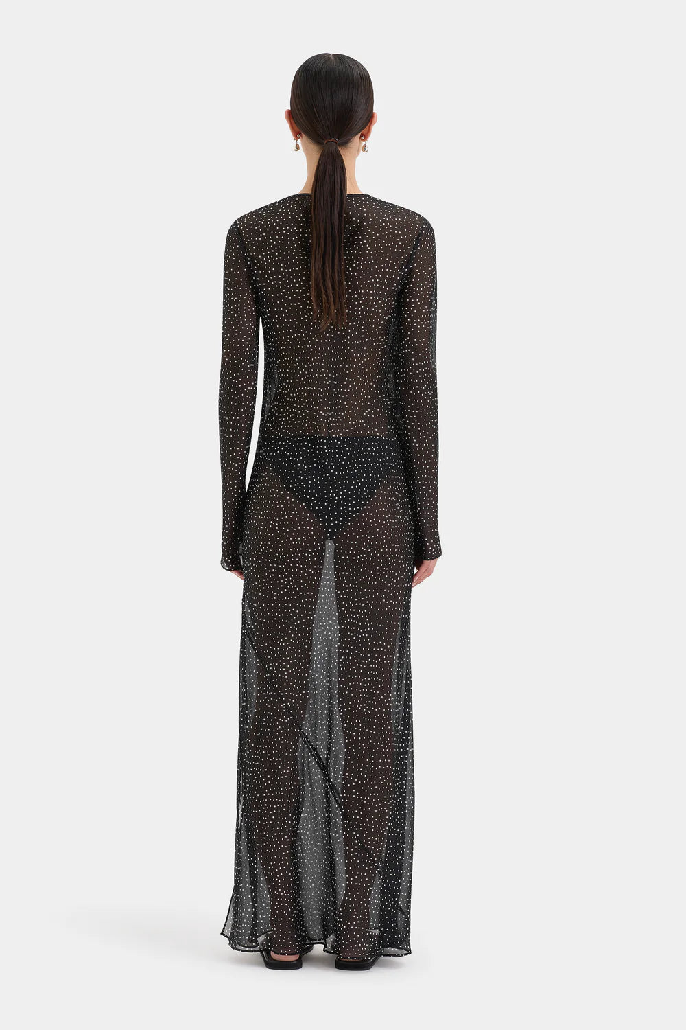 A model viewed from the back wearing a sheer, long-sleeved maxi dress with a black and brown animal print pattern, set against a plain light gray background.