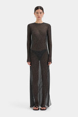 A model wearing a sheer, long-sleeved maxi dress with a dense black and brown abstract pattern, standing against a light gray studio background.
