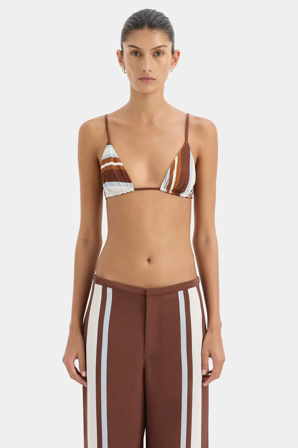 Woman wearing a brown and white striped bikini top with matching pants on a light gray background