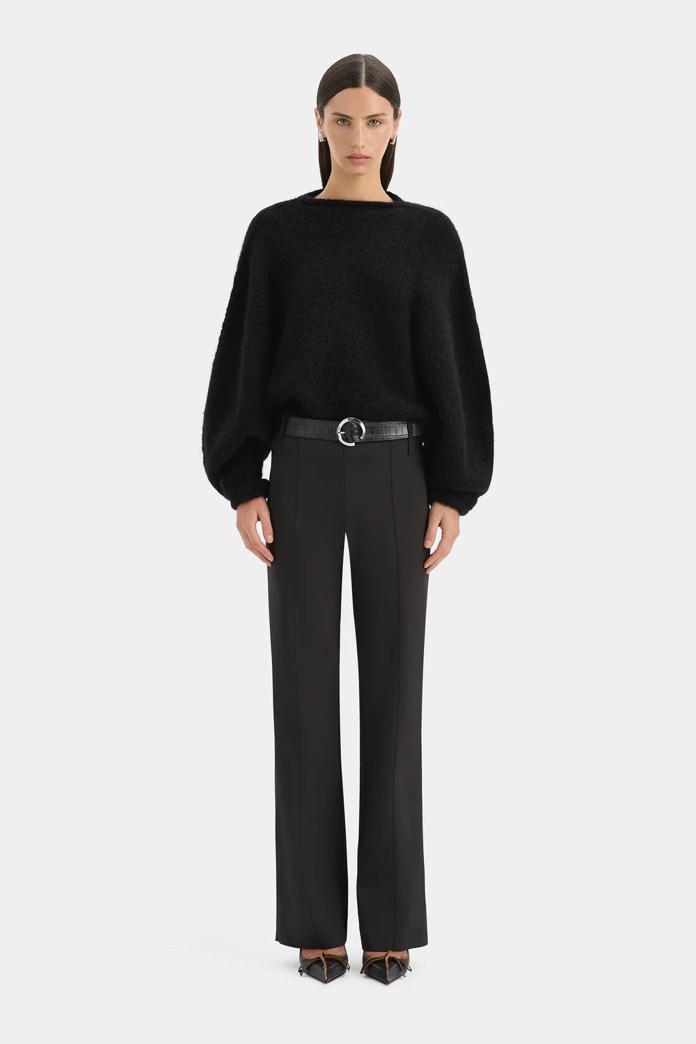 Person wearing a black sweater and black pants on a white background