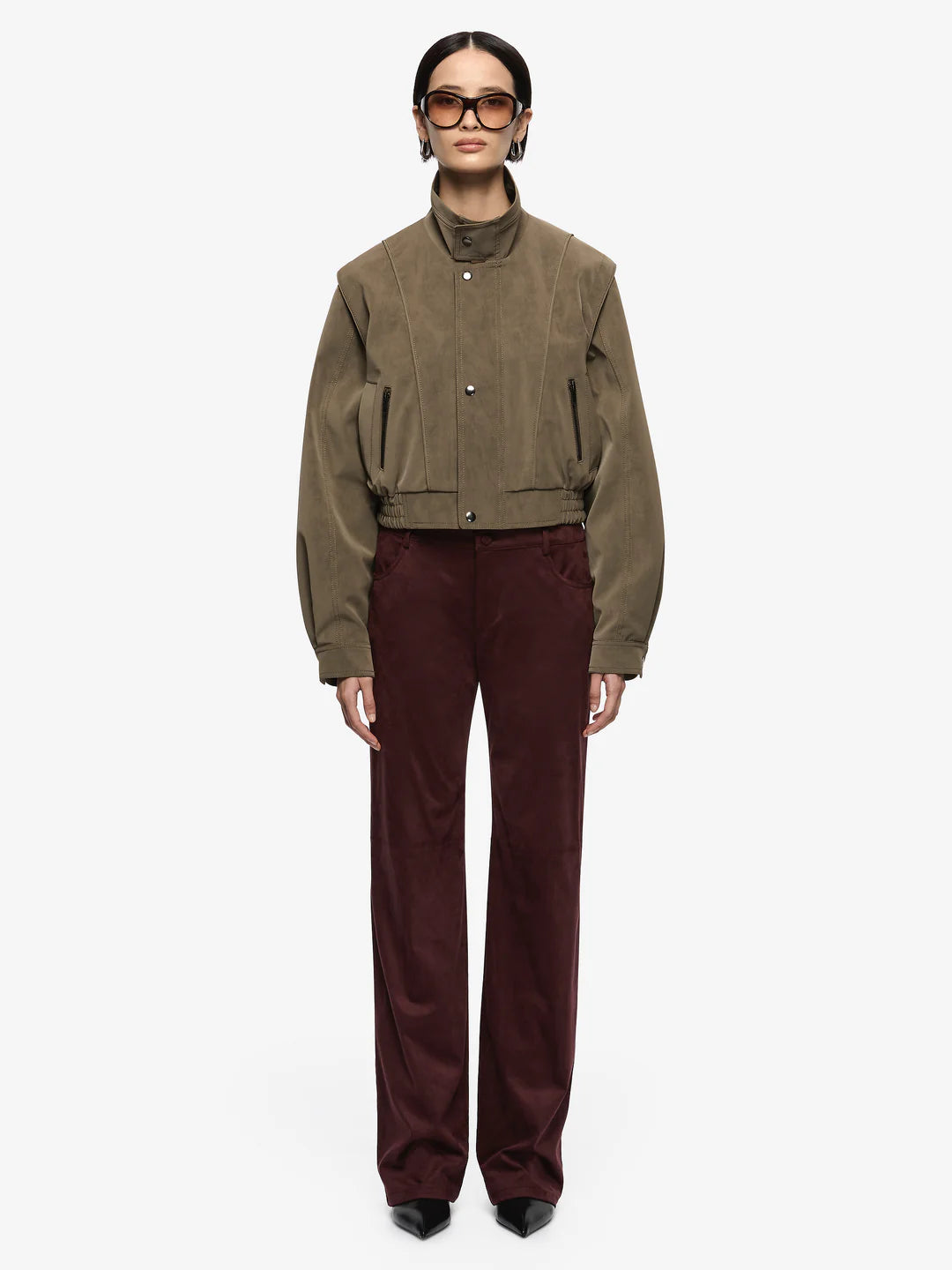 Zoli Bomber in Olive. A chic faux-suede bomber perfect for layering. Designed with panel detailing, internal wadding for warmth, elasticated waistband, and metal press-stud closures, combining structure with relaxed comfort.