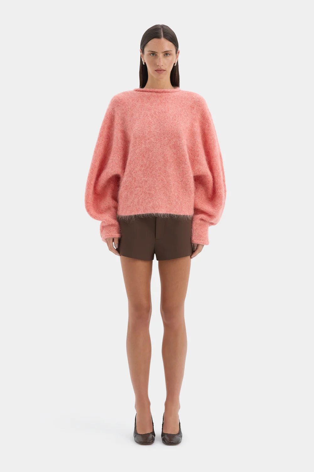 Woman wearing a pink sweater and brown shorts on a white background