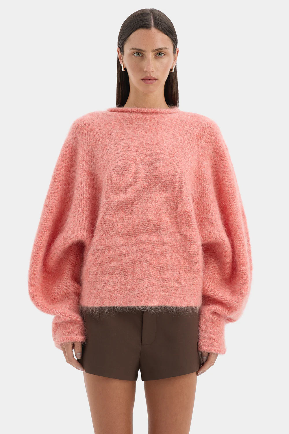 Person wearing a pink sweater and brown shorts on a white background