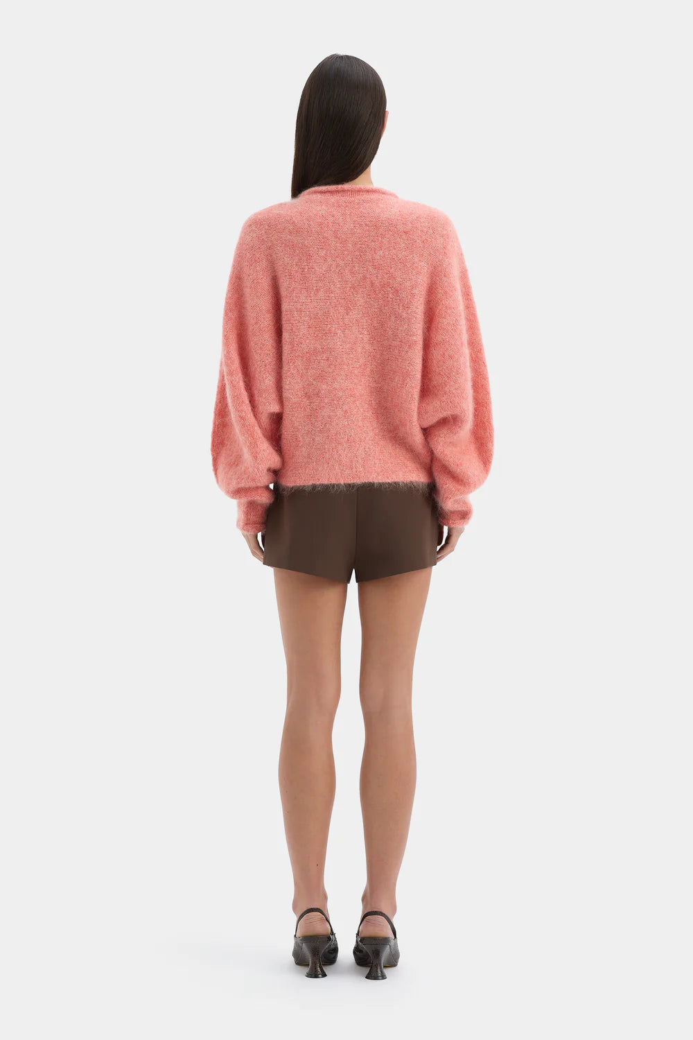 Person wearing a pink sweater and brown shorts on a white background