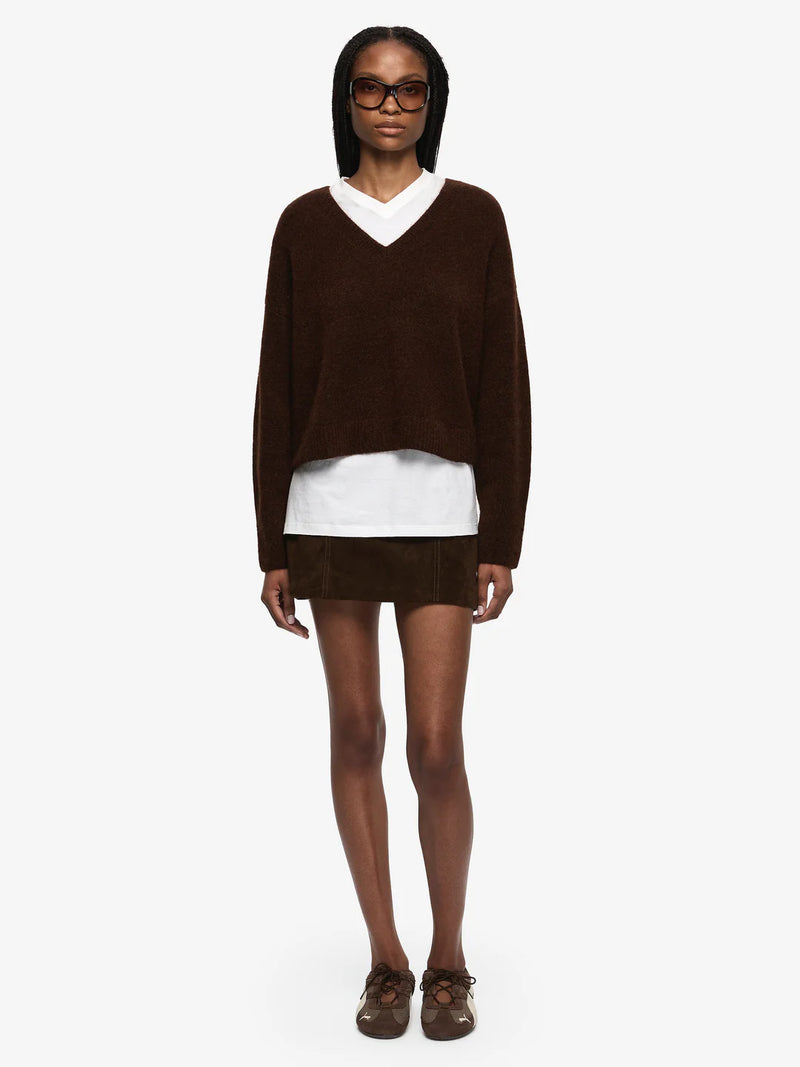 Person wearing a brown sweater over a white shirt with a white background