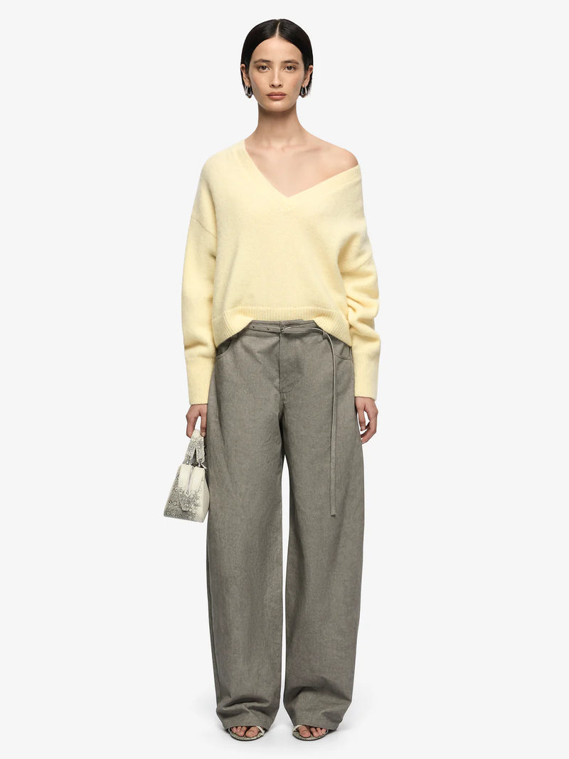 Woman wearing a yellow sweater and gray pants on a white background