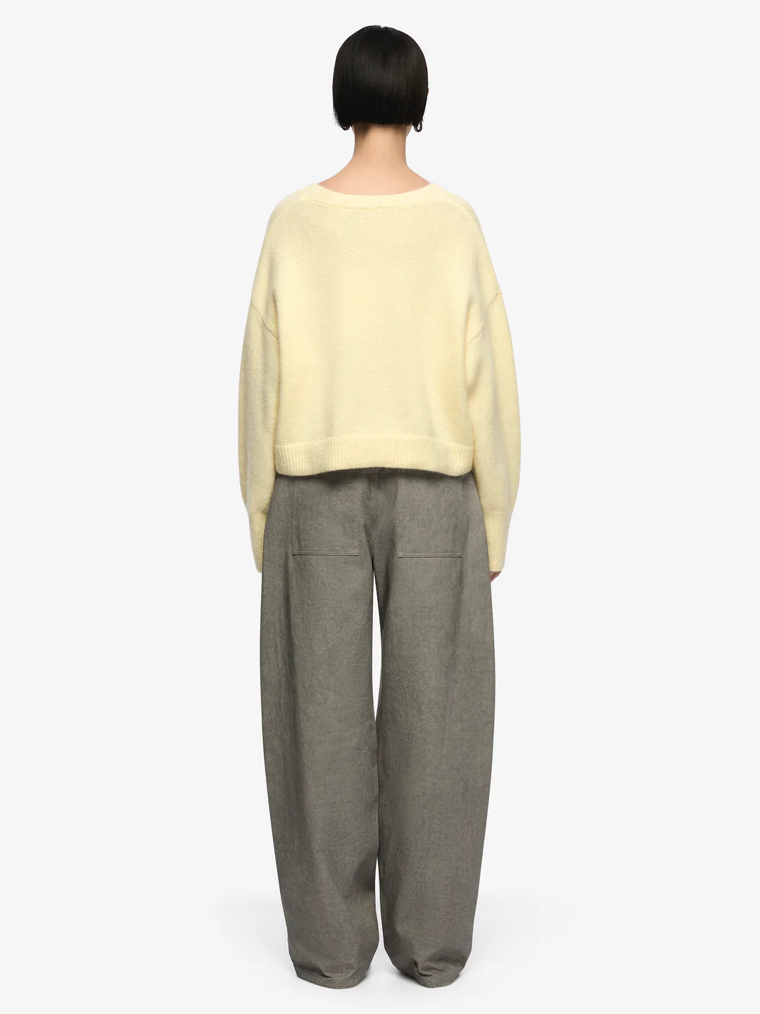 Person wearing a light yellow sweater and gray pants on a white background