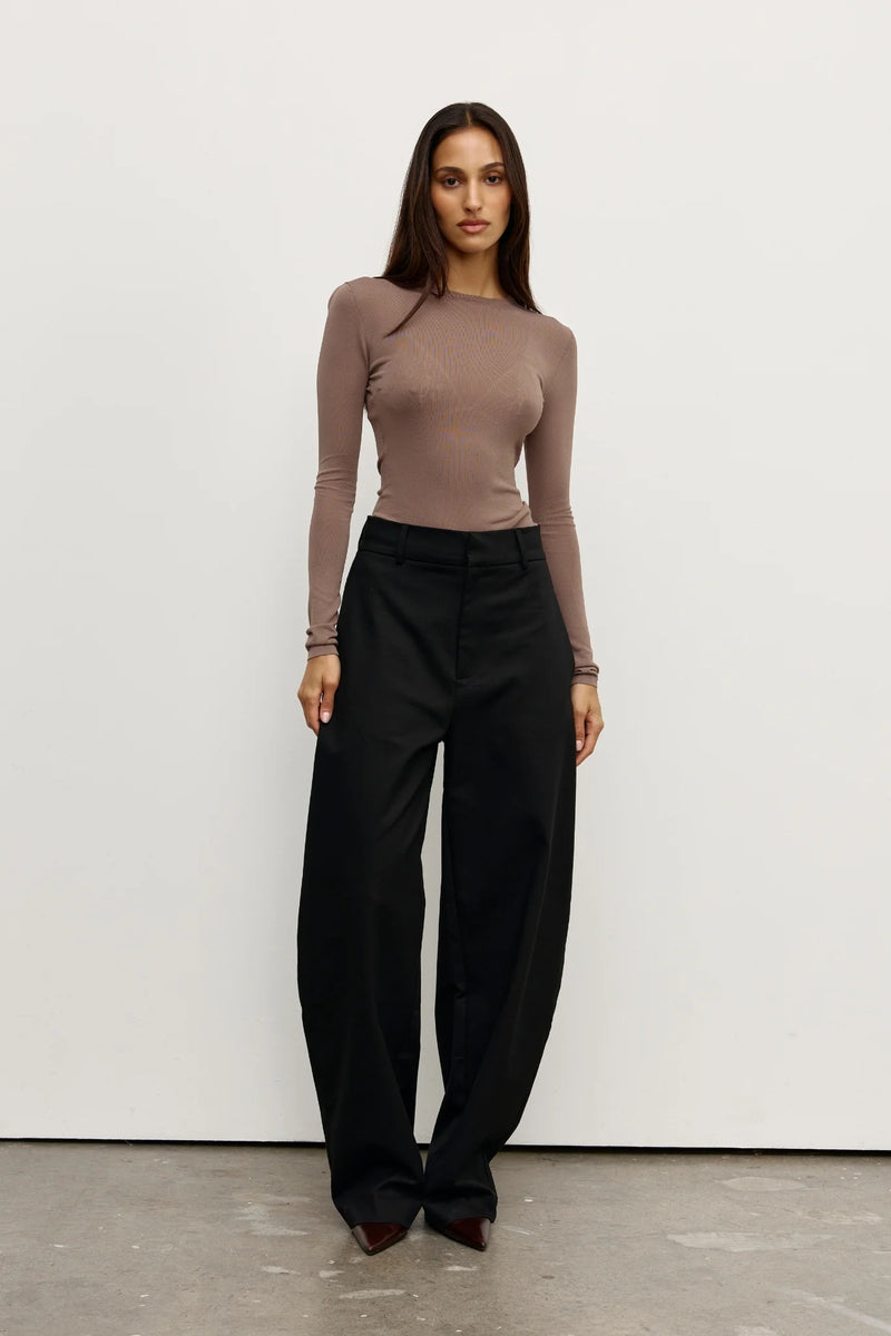 A woman in a brown fitted top with black pants on white background
