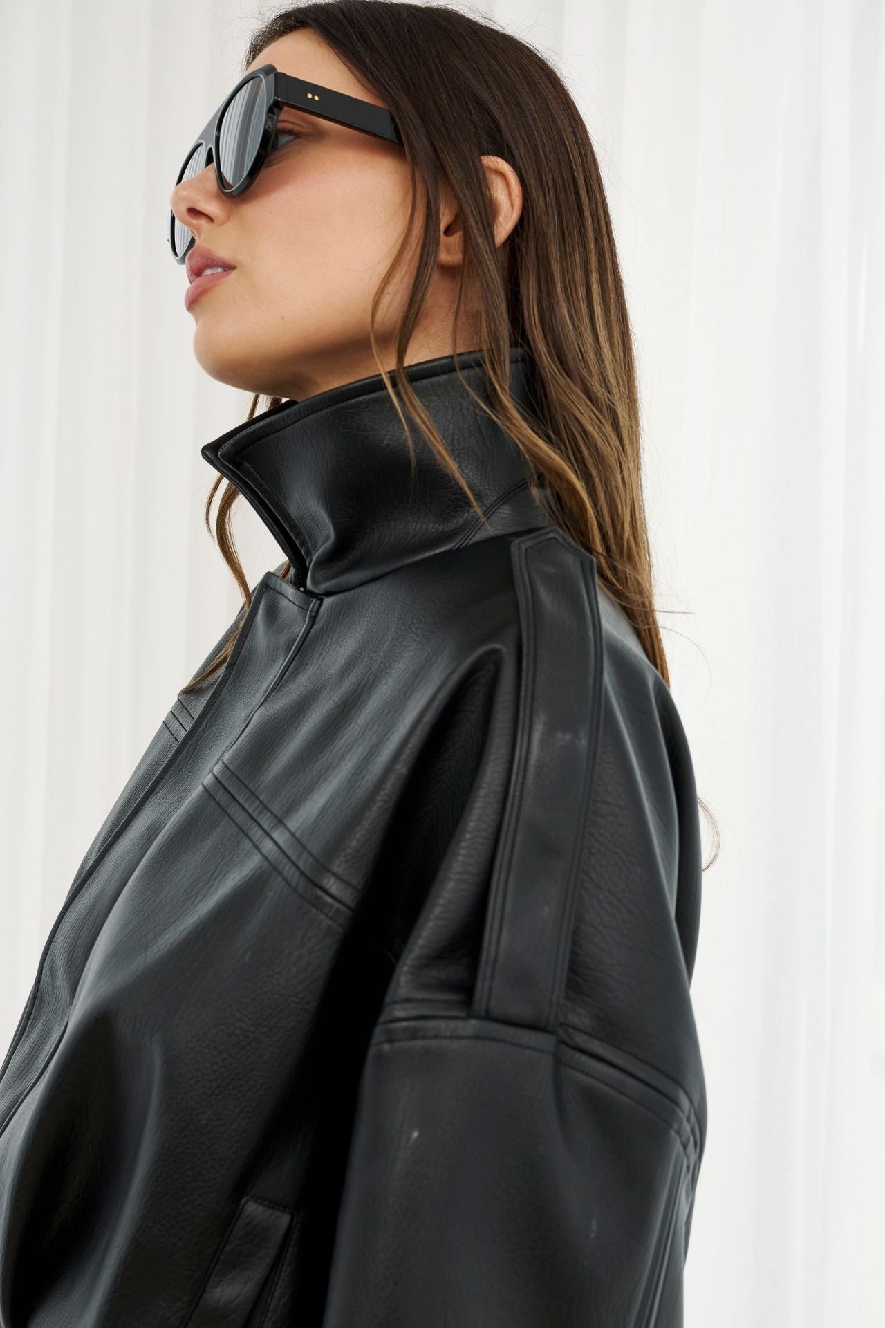 Woman wearing a black leather jacket and sunglasses against a white background