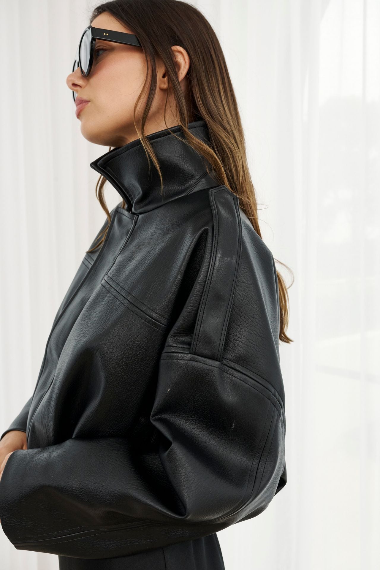 Woman wearing a black leather jacket and sunglasses against a white background