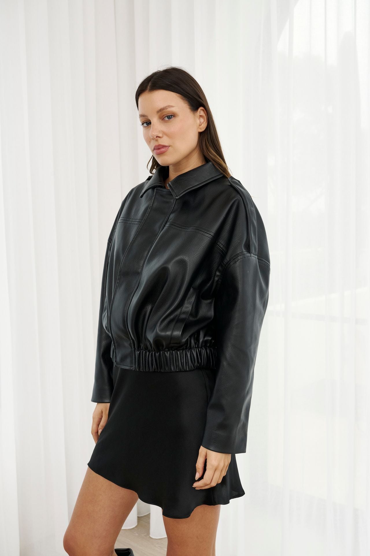 Woman wearing a black leather outfit against a white curtain background
