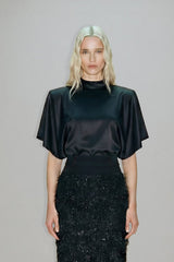 Person wearing a black top and black textured skirt against a gray background