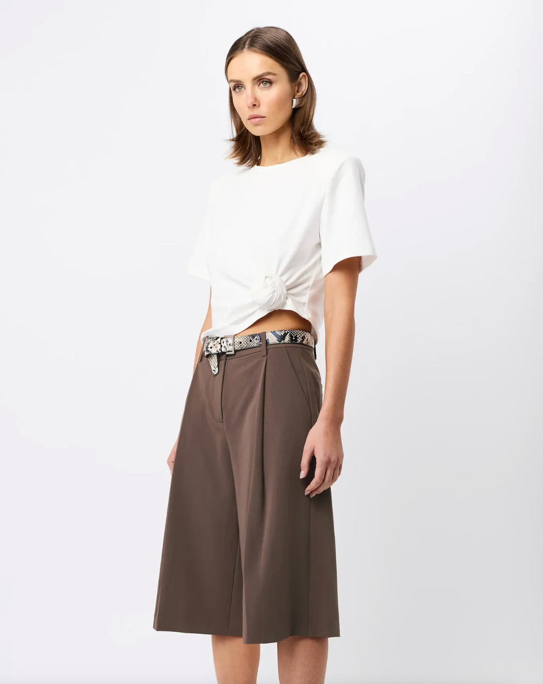 Woman wearing a white top and brown skirt with a belt on a white background