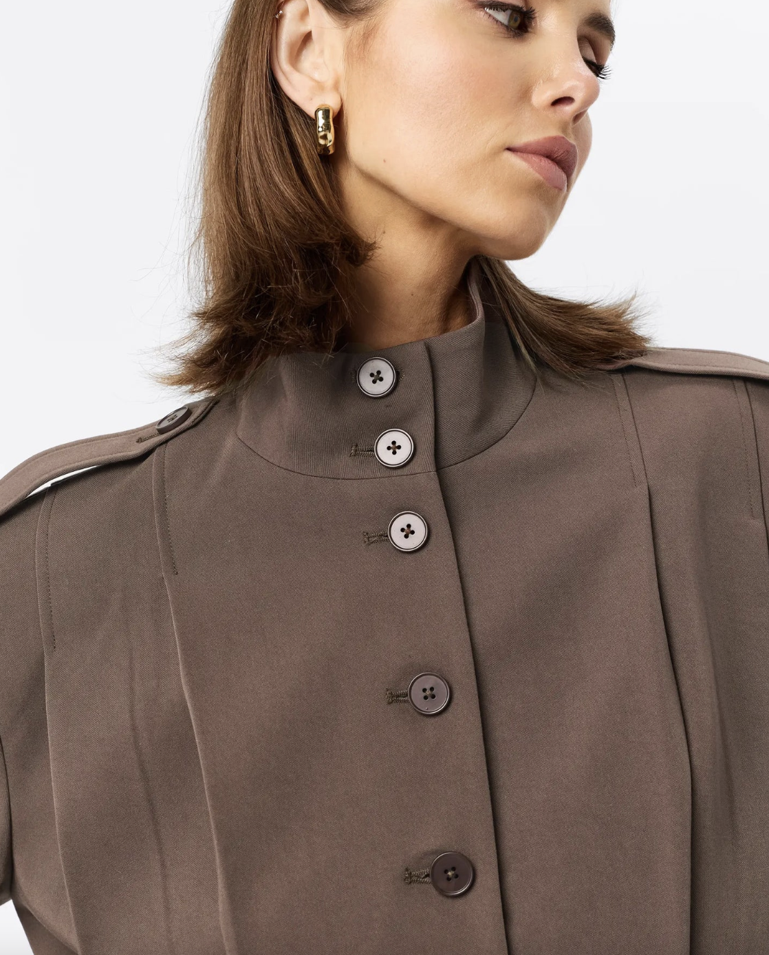 Close-up of a woman wearing a brown coat with button details on a white background
