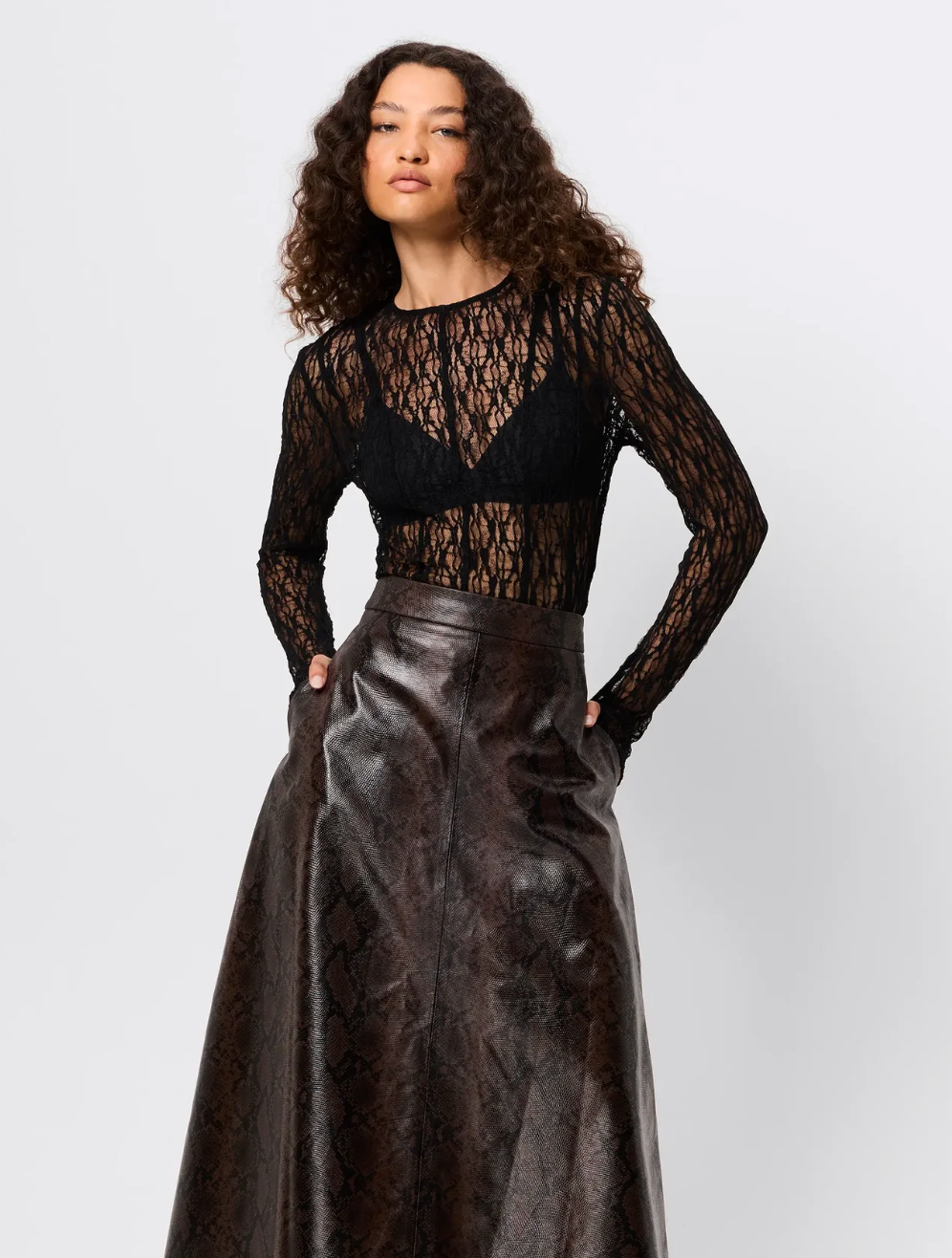 Woman wearing a black lace top and dark leather skirt on a white background
