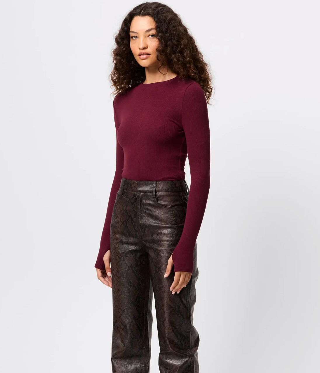 Woman wearing a burgundy long-sleeve top and black leather pants on a white background